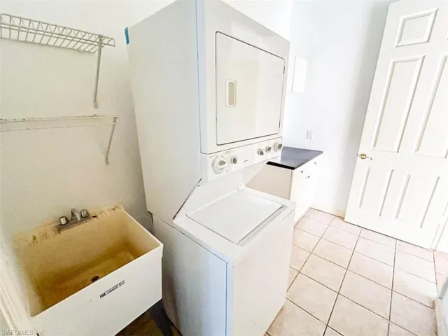 Laundry room featuring stacked washer / drying machine, sink, and light tile patterned flooring