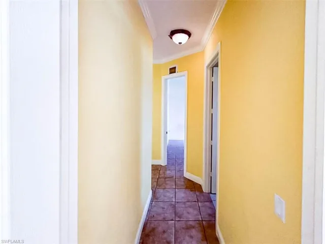 Corridor with dark tile patterned flooring and crown molding