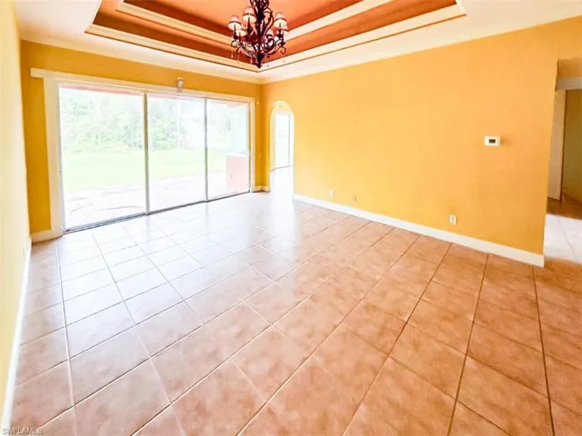 Tiled spare room featuring a tray ceiling, a notable chandelier, and ornamental molding
