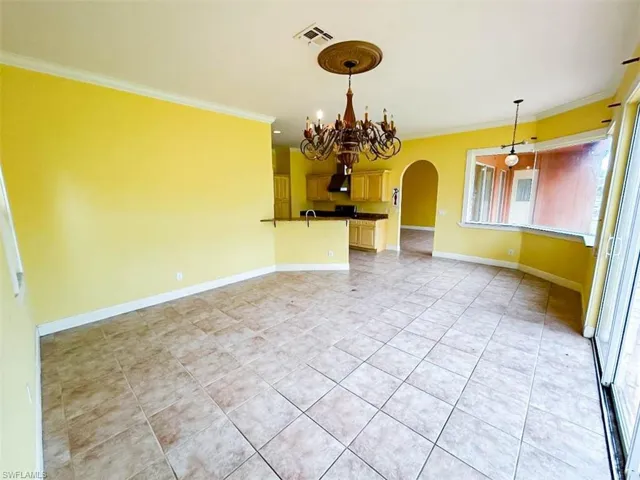 Unfurnished room featuring a notable chandelier, light tile patterned floors, and crown molding