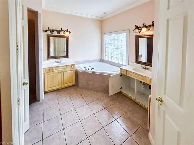 Bathroom featuring vanity, tile patterned floors, crown molding, and a relaxing tiled tub