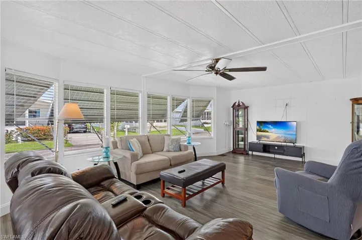 Spacious living area featuring expansive window treatments, wood-finish flooring, and a ceiling fan