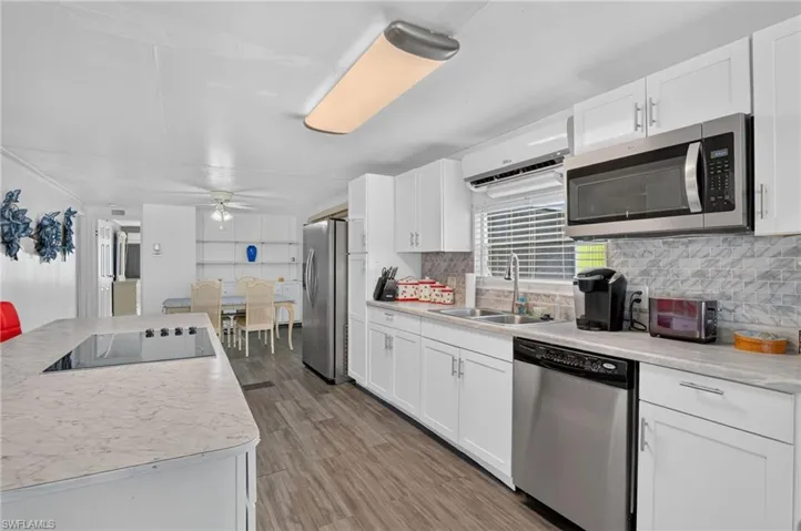 Spacious kitchen featuring white cabinetry, light countertops, wood-finish flooring, a stainless steel appliance suite, and a tile backsplash