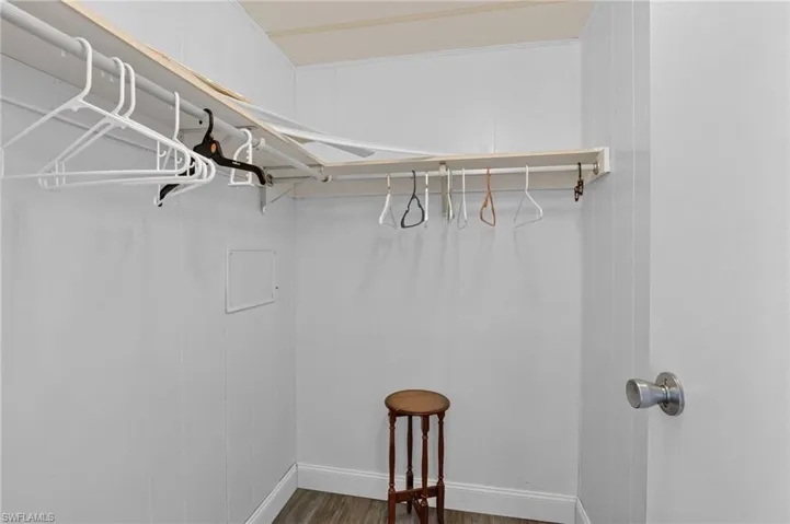 L-shaped closet with white paneled walls, wood-finish flooring, and a white door with a brushed nickel knob