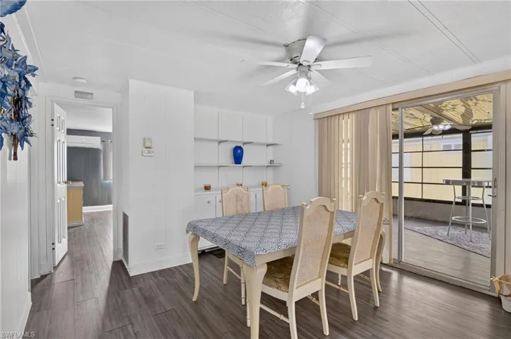 Dining area featuring wood-finish flooring, built-in shelving, a ceiling fan with integrated lighting, and sliding glass doors opening to an enclosed patio