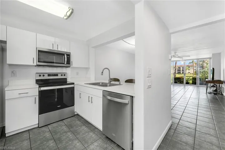 Kitchen with appliances with stainless steel finishes, dark tile patterned flooring, light countertops, and white cabinetry