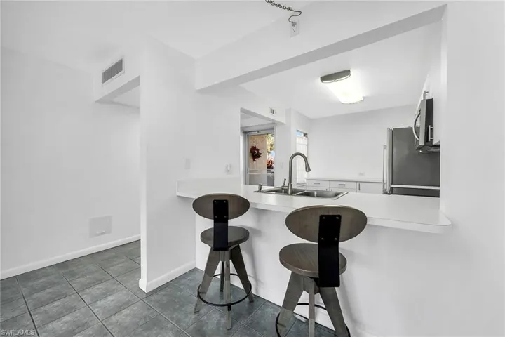 Kitchen featuring a breakfast bar, light countertops, white cabinetry, a peninsula, and stainless steel microwave