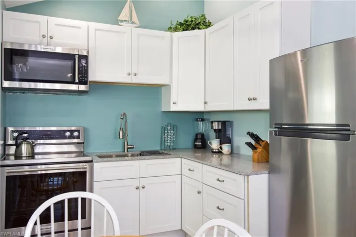 Kitchen with white cabinetry, appliances with stainless steel finishes, and light stone countertops - Virtually Edited Image
