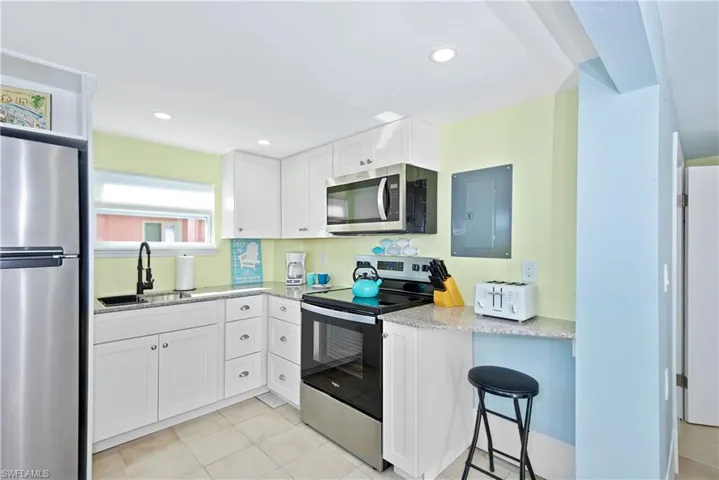 Kitchen featuring stainless steel appliances, light stone countertops, white cabinetry, electric panel, and light tile patterned floors - Virtually Edited Image