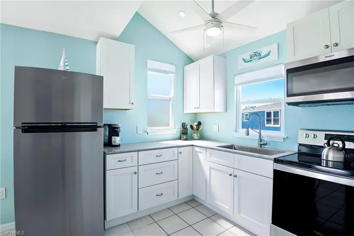 Kitchen featuring stainless steel appliances, white cabinetry, light tile patterned floors, a ceiling fan, and vaulted ceiling - Virtually Edited Image