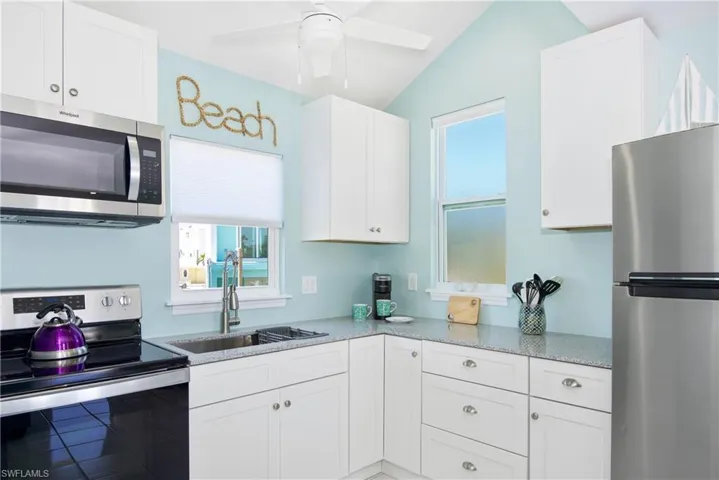 Kitchen featuring stainless steel appliances, plenty of natural light, white cabinetry, and lofted ceiling - Virtually Edited Image