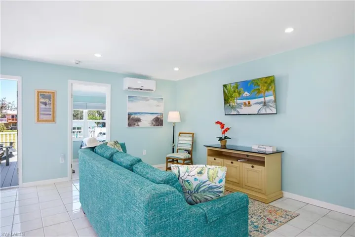 Living room with light tile patterned floors, recessed lighting, and a wall mounted air conditioner - Virtually Edited Image