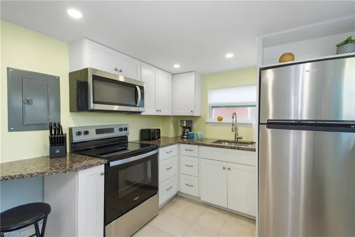 Kitchen featuring appliances with stainless steel finishes, electric panel, white cabinets, light tile patterned flooring, and recessed lighting - Virtually Edited Image