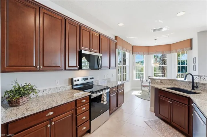 Kitchen with stainless steel appliances, light stone countertops, hanging light fixtures, and light tile patterned flooring