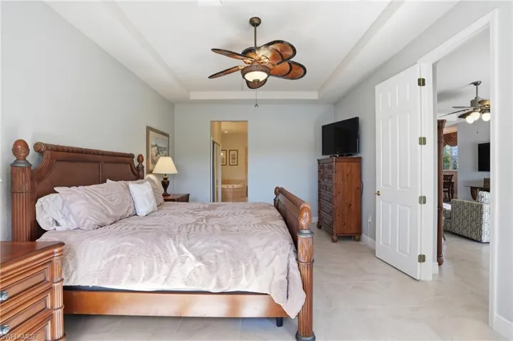 Bedroom with ensuite bath, a raised ceiling, and a ceiling fan