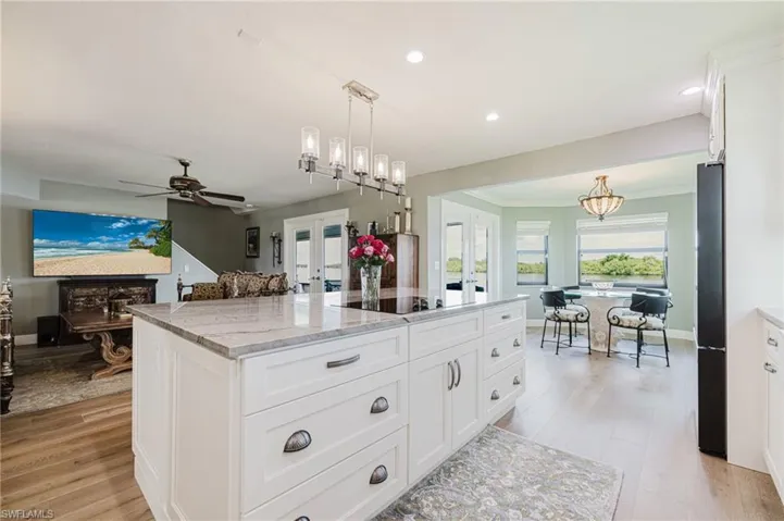 Kitchen with white cabinetry, light wood flooring, hanging light fixtures, light stone counters, and open floor plan