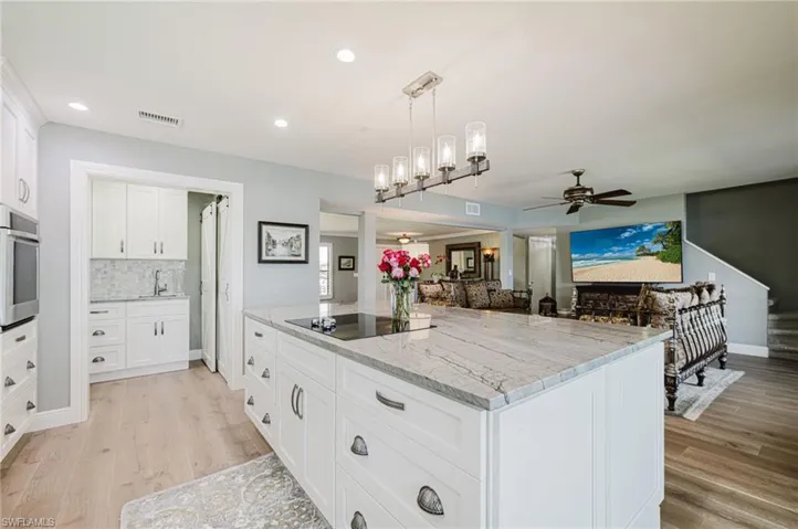 Kitchen with white cabinets, decorative light fixtures, light stone counters, a kitchen island, and light wood finished floors