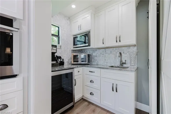 Kitchen with wine cooler, white cabinets, light stone counters, and recessed lighting