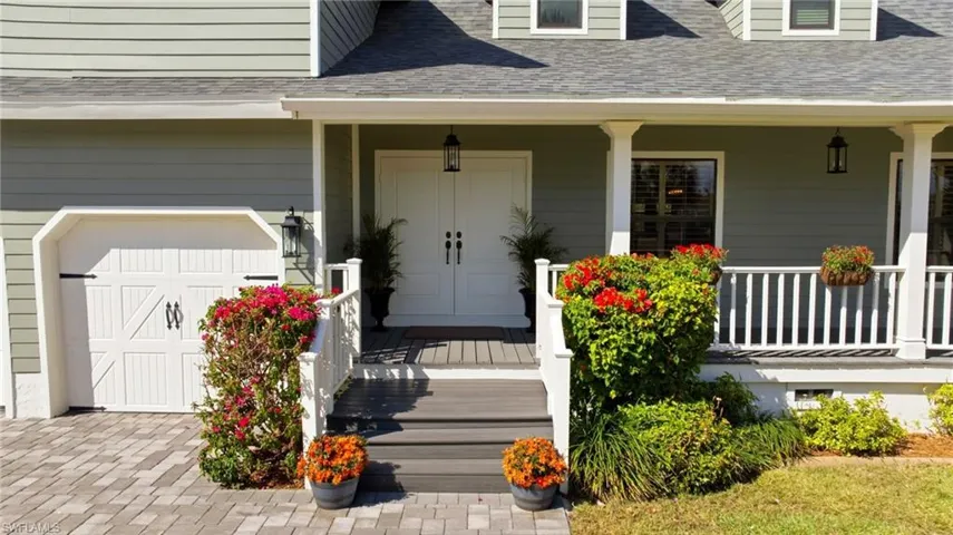 Doorway to property with covered porch, a shingled roof, and an attached garage