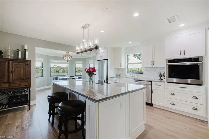 Kitchen with light stone counters, stainless steel appliances, a kitchen bar, light wood finished floors, and backsplash