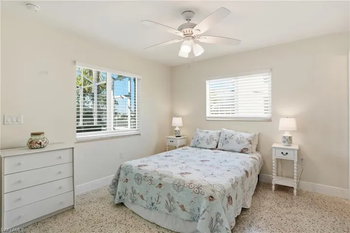 Bedroom featuring multiple windows, a ceiling fan, and dark aggregate flooring - Virtually Edited Image
