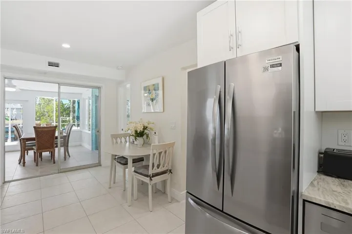Kitchen with freestanding refrigerator, light tile patterned flooring, white cabinets, recessed lighting, and light stone counters - Virtually Edited Image