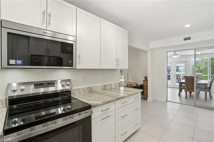 Kitchen with stainless steel appliances, white cabinets, healthy amount of natural light, light tile patterned flooring, and recessed lighting - Virtually Edited Image