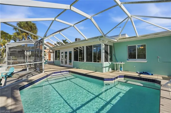 Outdoor pool with glass enclosure, a patio area, a sunroom, and french doors - Virtually Edited Image