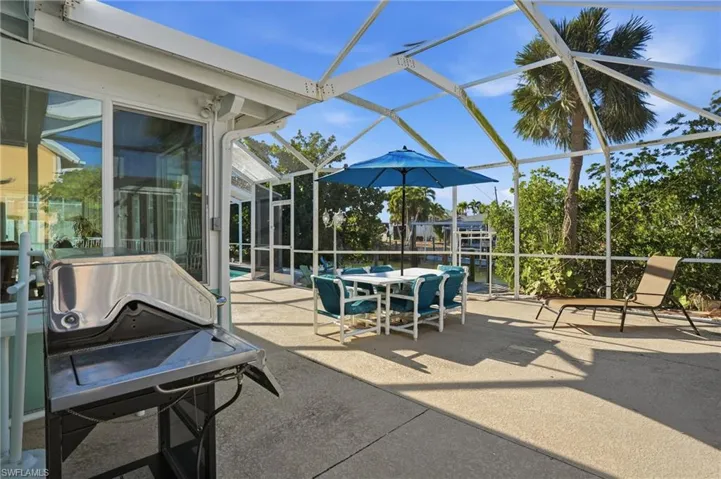 View of patio featuring glass enclosure, a sunroom, a grill, and outdoor dining space - Virtually Edited Image