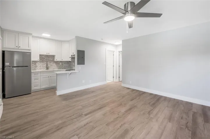 Unfurnished living room with light wood finished floors, electric panel, a sink, baseboards, and a ceiling fan