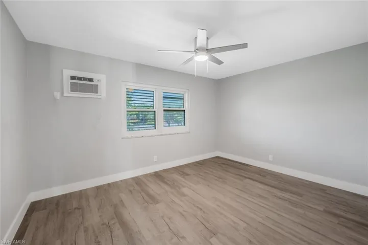 Unfurnished room with baseboards, a ceiling fan, wood finished floors, and a wall unit AC