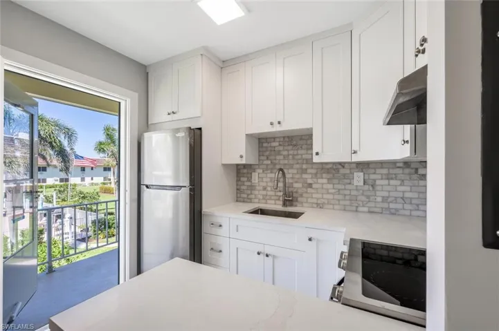 Kitchen featuring under cabinet range hood, backsplash, a sink, freestanding refrigerator, and range