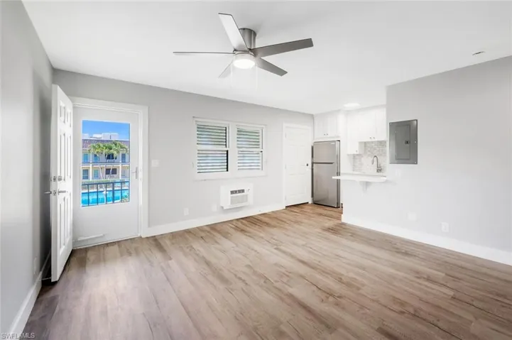 Unfurnished living room with an AC wall unit, baseboards, a ceiling fan, and light wood-type flooring
