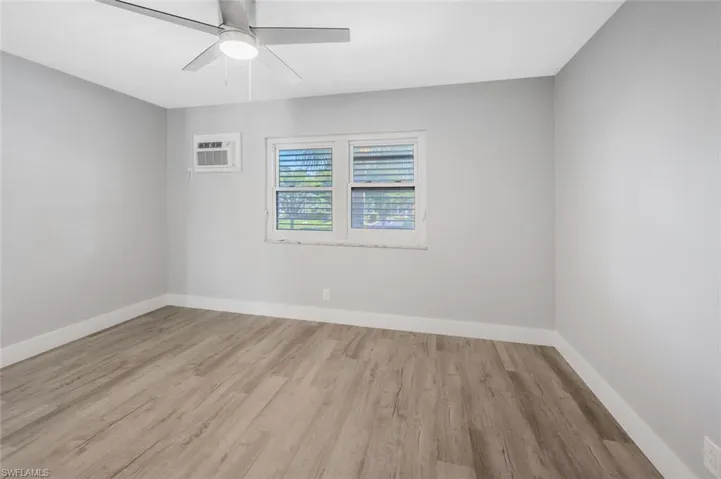Unfurnished room featuring baseboards, a ceiling fan, wood finished floors, and a wall mounted air conditioner