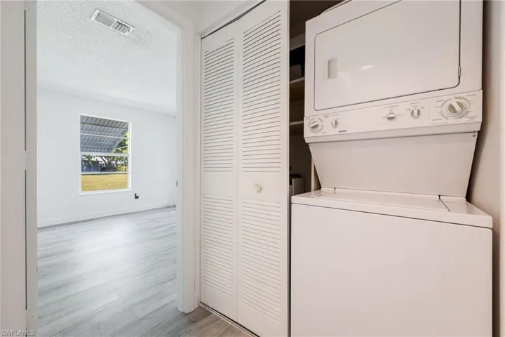Laundry area featuring a textured ceiling, stacked washer and clothes dryer, and light wood-type flooring