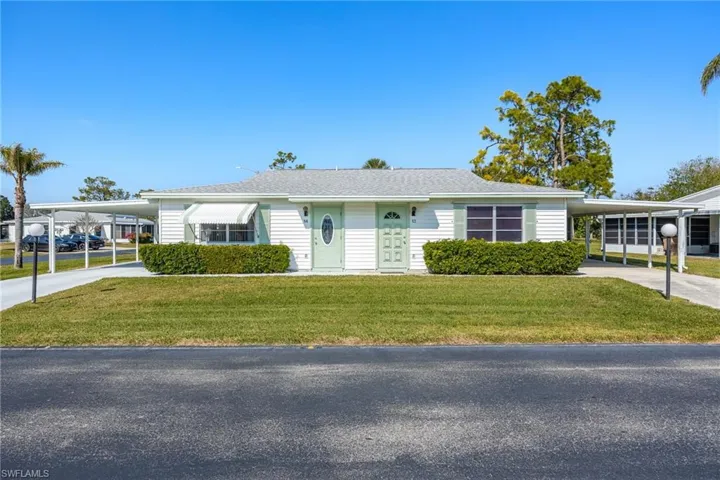 Ranch-style house with an attached carport, driveway, a front yard, and roof with shingles