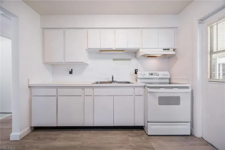 Kitchen with white electric range, light countertops, and white cabinets