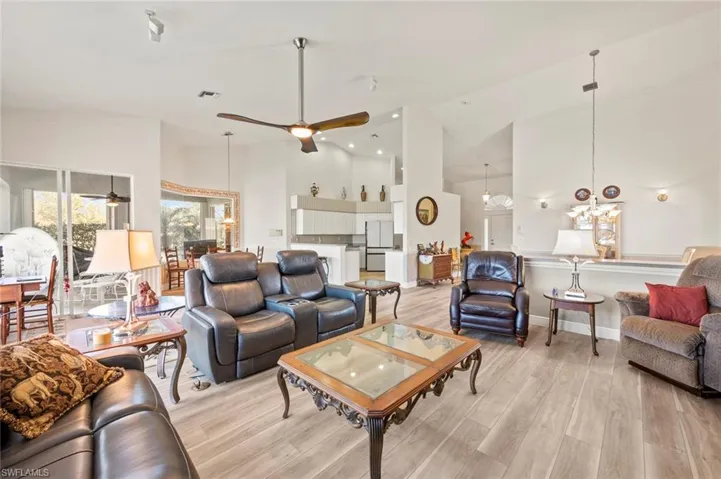 Living room with high vaulted ceiling, ceiling fan with notable chandelier, and light hardwood / wood-style floors