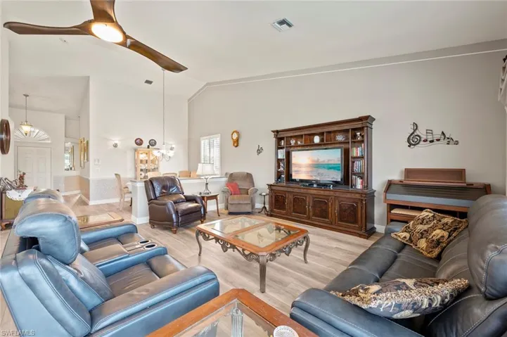 Living room featuring ceiling fan with notable chandelier, vaulted ceiling, and light hardwood / wood-style flooring