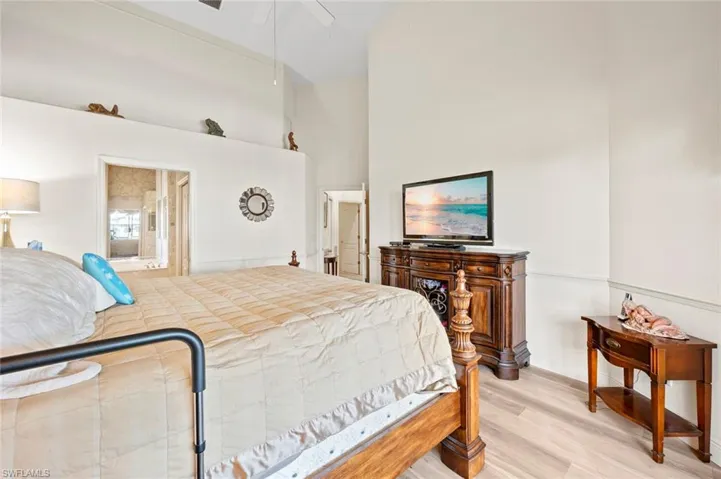 Bedroom with connected bathroom, a towering ceiling, light hardwood / wood-style floors, and ceiling fan