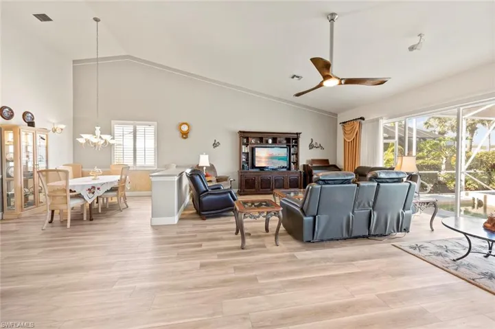 Living room with ceiling fan with notable chandelier, high vaulted ceiling, and light wood-type flooring