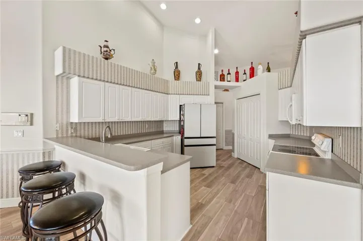 Kitchen featuring white appliances, tasteful backsplash, light hardwood / wood-style floors, white cabinets, and kitchen peninsula
