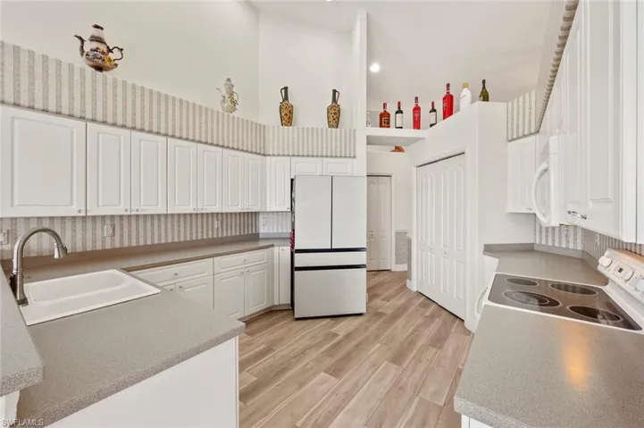 Kitchen with sink, white cabinets, a high ceiling, white appliances, and light hardwood / wood-style flooring