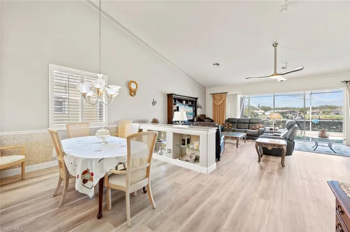 Dining space with high vaulted ceiling, ceiling fan with notable chandelier, and light hardwood / wood-style floors