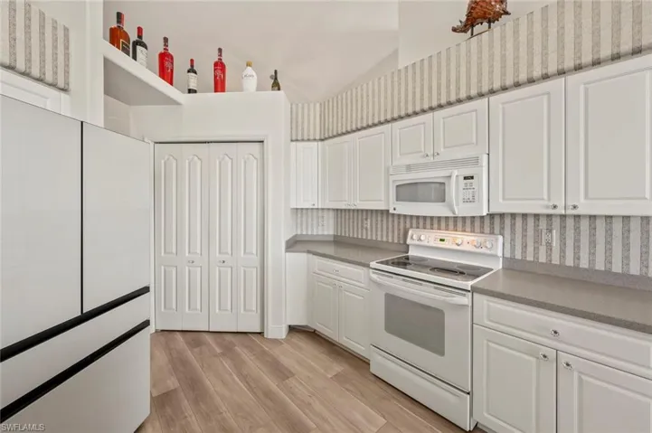 Kitchen with white cabinetry, light wood-type flooring, and white appliances