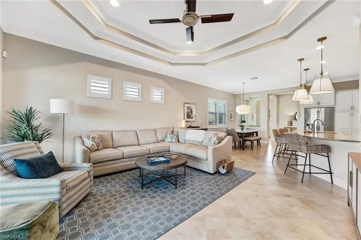 Living room featuring ornamental molding, a ceiling fan, a tray ceiling, light tile patterned floors, and recessed lighting