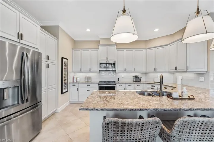 Kitchen featuring stainless steel appliances, light stone countertops, a peninsula, a kitchen bar, and crown molding