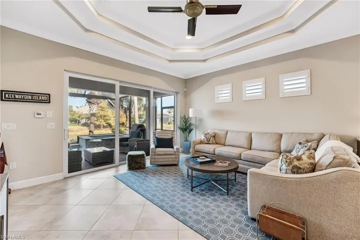 Tiled living room with ornamental molding, ceiling fan, and a tray ceiling
