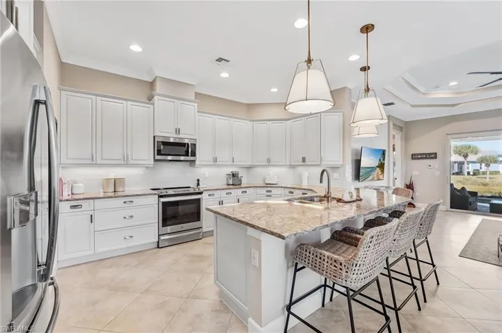 Kitchen featuring appliances with stainless steel finishes, light stone counters, hanging light fixtures, a kitchen breakfast bar, and backsplash