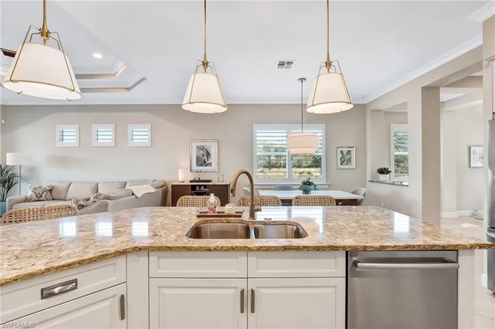 Kitchen featuring open floor plan, dishwasher, light stone counters, hanging light fixtures, and white cabinetry